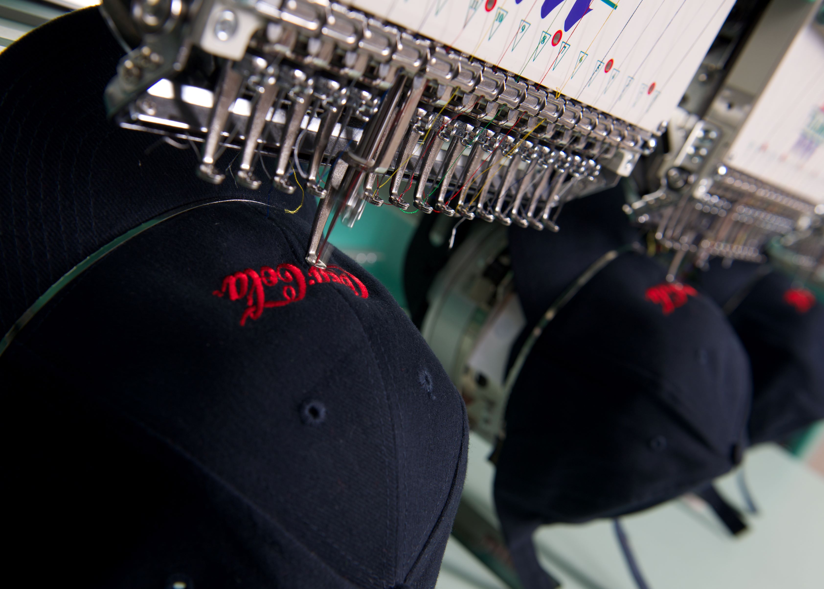 Close-up of embroidery machine stitching branded logos onto caps