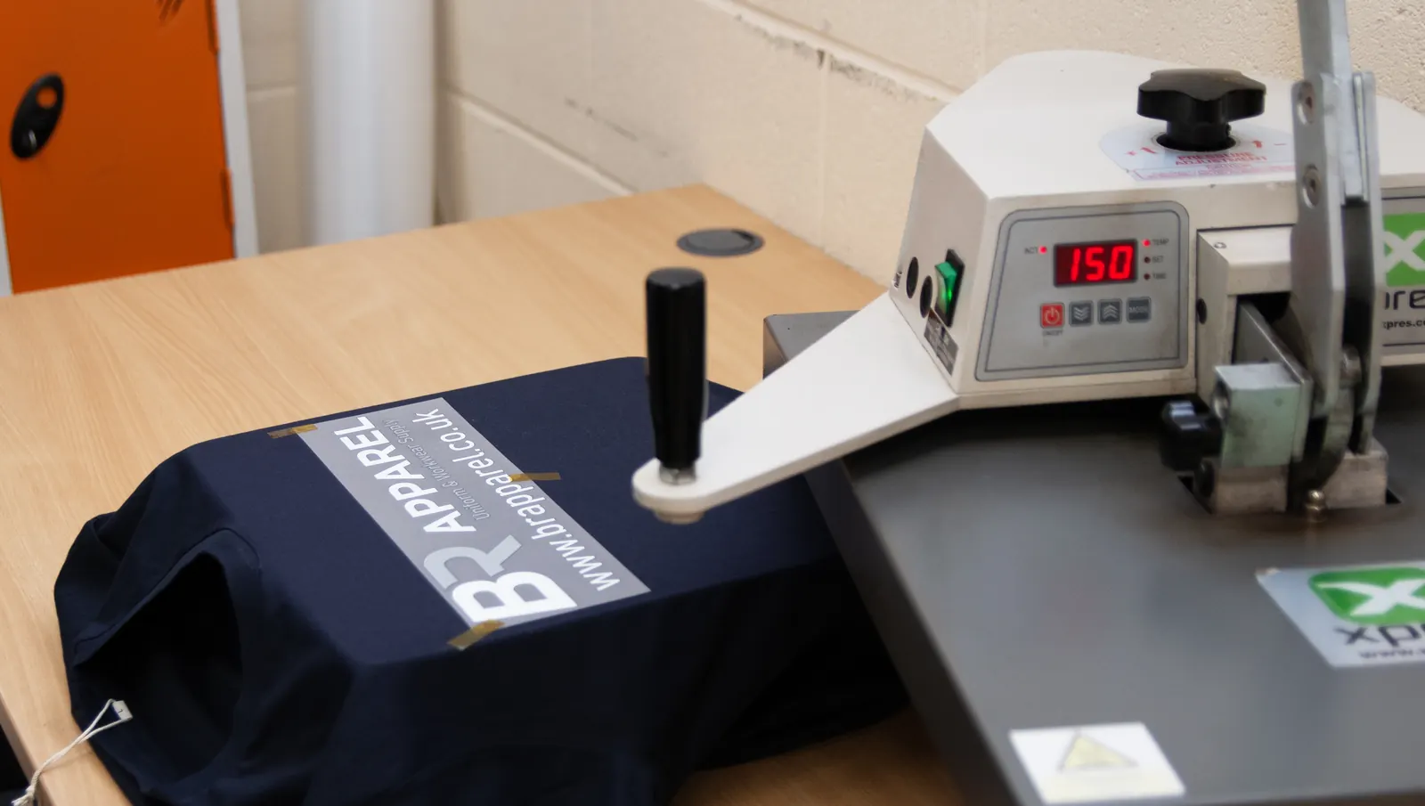 Heat press applying a printed transfer to a navy garment at BR Apparel