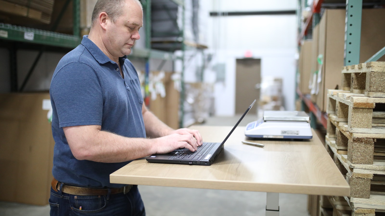 Warehouse team member in a branded polo working at a stand-up desk on the floor