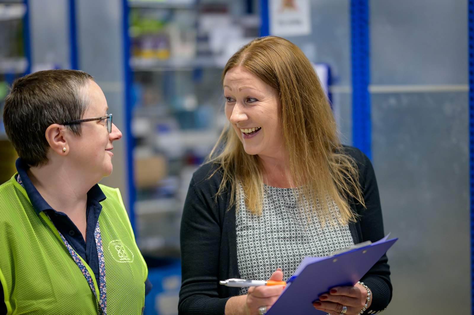 Warehouse supervisor in branded hi-vis vest talking with a manager on the floor
